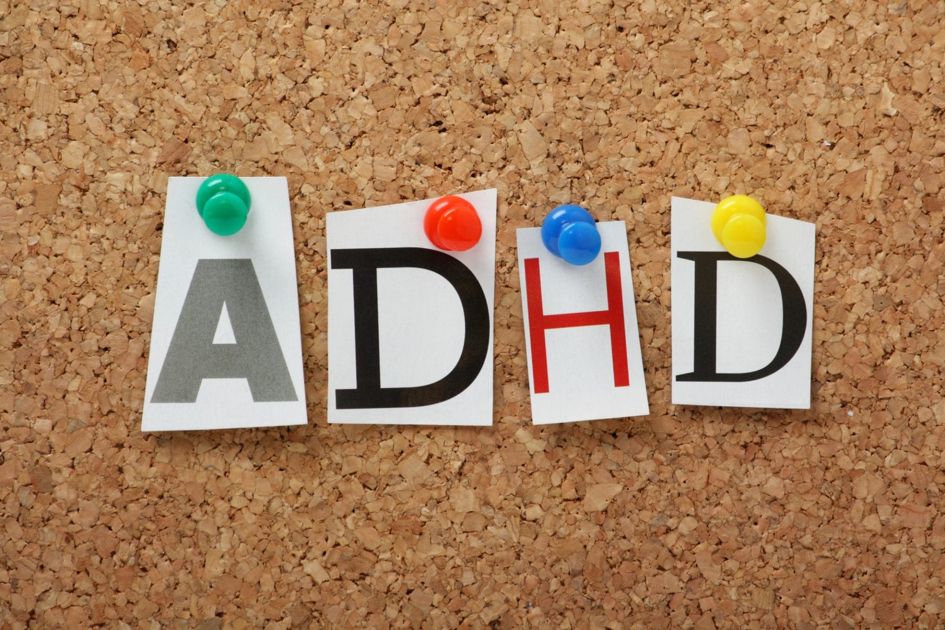 Letters "adhd" pinned on a corkboard with colorful pushpins.