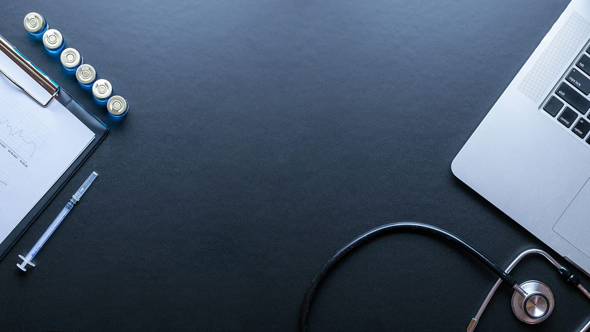 A stethoscope, laptop, clipboard with paper, and batteries arranged on a dark surface.