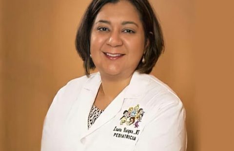 A professional portrait of a smiling pediatrician wearing a white lab coat with an embroidered name and title.