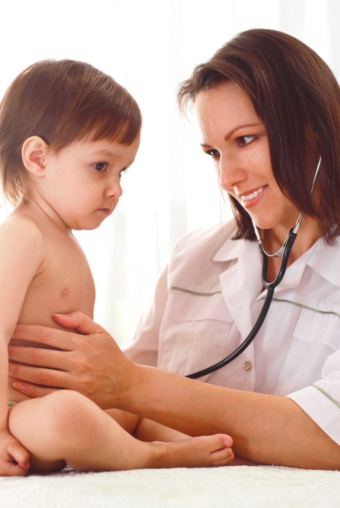 A medical professional using a stethoscope to listen to a child's chest during an examination.