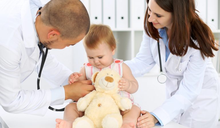 Two pediatricians interacting with a baby patient holding a stuffed toy. Two pediatricians interacting with a baby patient holding a stuffed toy.