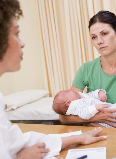 A mother holding her baby during a consultation with a healthcare professional.