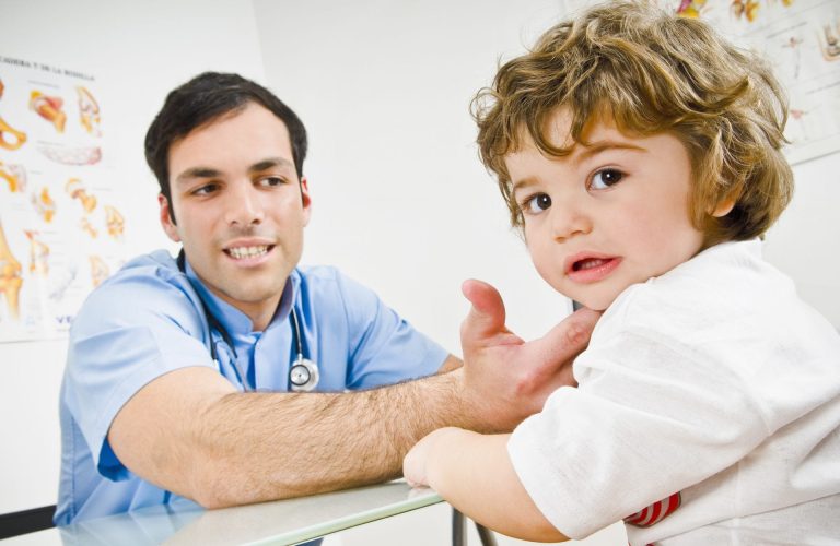 A healthcare professional extends his hand toward a young child in a clinical setting.